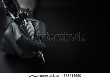 Tattoo artist holding tattoo machine on dark background with space for text