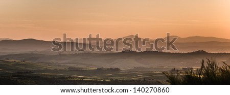 Panoramic view on fields in Tuscan landscape colored by the setting sun with clear silhouette of the mountains in the background