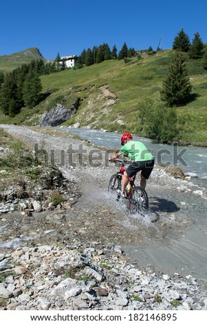 Mountain biker riding through stream in Swiss mountain area with water splashing