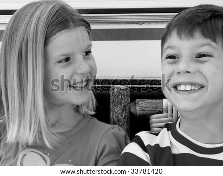 Young girl looking at her brother as he practices his smile. Focus is on young girl with slight movement of boy.