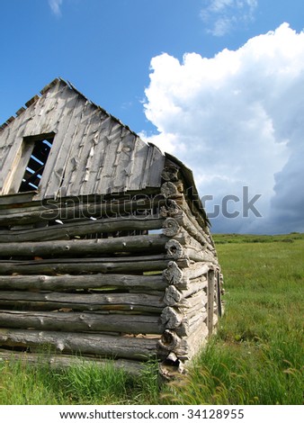 Abandoned cabin in green field with storm approaching.