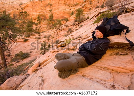 Man dressed in warmer clothing resting with his eyes closed after hiking in Zion National Park, Utah, USA. Late Autumn.
