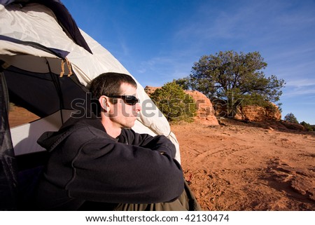 Wide angle view of young man sitting inside tent in Arizona desert. Outdoor adventure/camping concept.