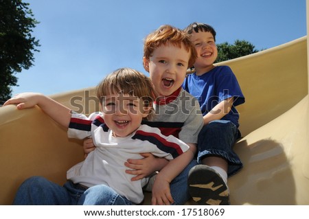 Three brothers have a great time sliding down a spiral slide on a neighborhood schoolyard