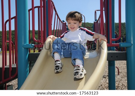 A toddler shows his excitement as he is about to take off on a slide in a neighborhood playground