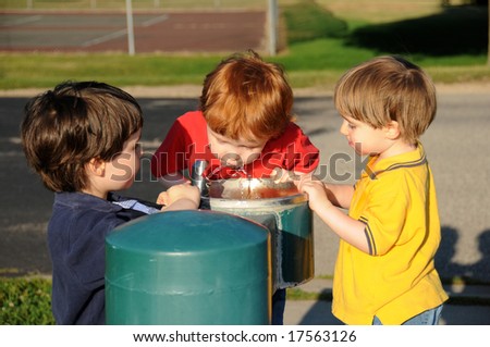 Three brothers take turns drinking water from a drinking fountain at a neighborhood park.