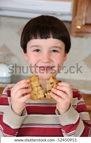 A little boy smiles as he breaks a chocolate chip cookie before eating it