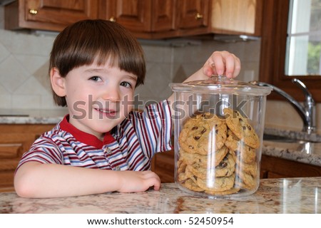 A little boy steals chocolate chip cookies from a cookie jar in his mother\'s kitchen