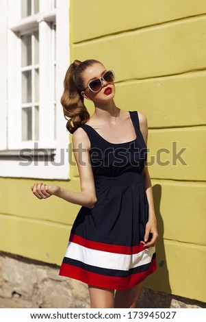 Beautiful woman in sunglasses and colorful dress Fashion model in sunglasses. Pin up style. Sixties and fifties. Colorful dress. Yellow wall. Vogue style.