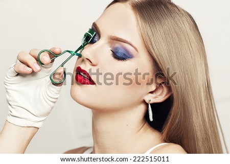 Beautiful woman with closed eyes holding eyelash curler. Evening make up. Portrait of young model. Red lips.