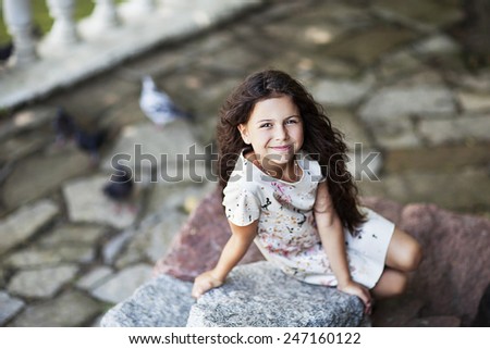 Beautiful girl sitting on the rock. Girl smiling on the street. Green park. warm shiny weather. Young happy girl.