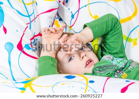 young boy is covering his eyes while lying on multicolored sitting bag