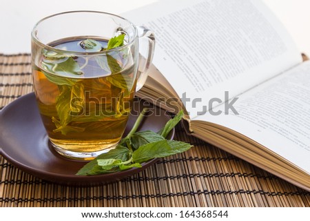Green tea and leaves of mint in a glass cup on a bamboo mat with an open book