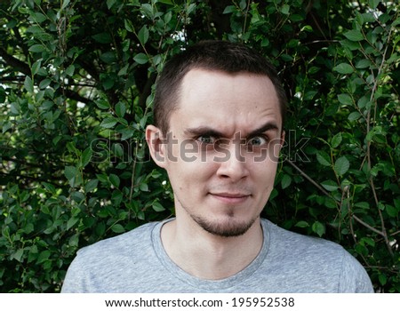 Man standing outdoors in front of green foliage raising an eyebrow in total disbelief and distrust glaring at the camera with an intense stare