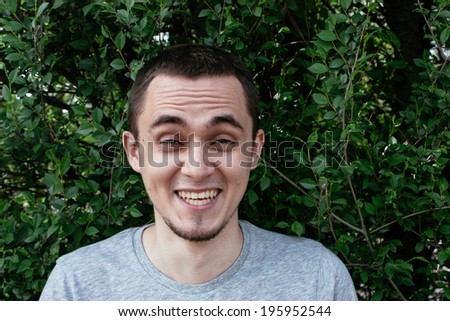 Young man with a goatee beard having a good laugh at a funny joke raising his eyebrows in mirth, standing against a leafy green tree