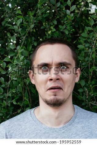 Terrified man staring aghast at the camera with wide fearful eyes and a penetrating stare against a background of green leaves