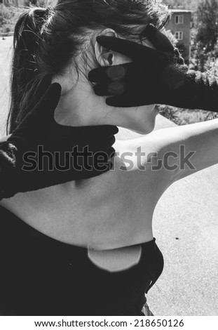 Dramatic suggestive portrait of an elegant young woman in an off-the-shoulder dress holding her gloved hands to her throat and face conceptual of coercion and violence or as a diva seeking attention