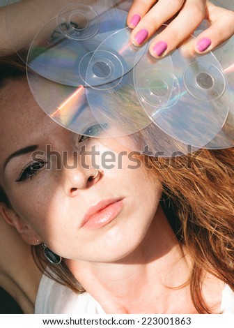 Sensual woman holding up CD discs to the sunlight in front of her face while giving the camera a sultry seductive look