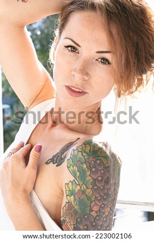 Attractive young woman displaying a colorful arm tattoo as she lowers the shoulder of her summer top