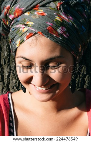 Close up Pretty Smiling Woman with Fashion Head Cover Leaning on Tree and Looking Down.