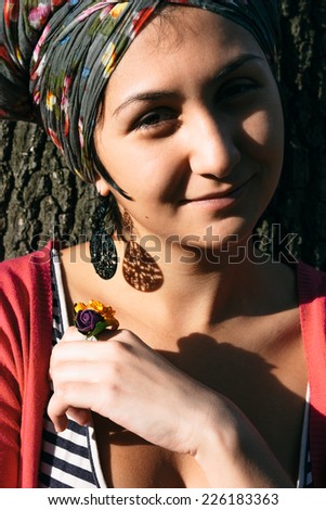 Close up Smiling Attractive Woman in Floral Head Cover and Finger Ring, Leaning to the Tree Trunk While Looking at the Camera.