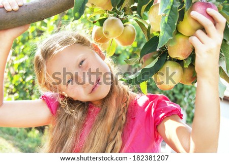 Portrait of happy smiling cute child (girl) near apple tree on beautiful day. Kid has healthy food outside in summer dress. Outdoor. Close up.