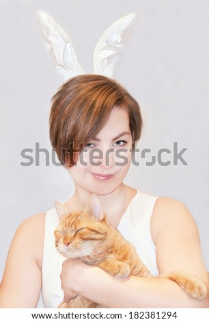 Portrait of a young woman, wearing easter bunny ears, with a cat . Indoor.