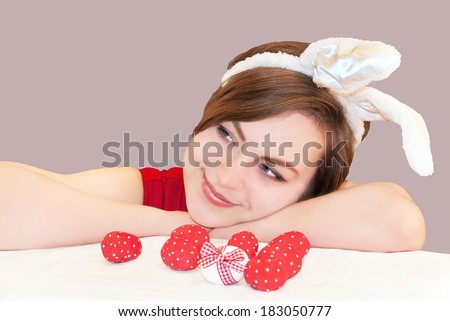 Portrait of a young woman wearing easter bunny ears. Easter eggs near her. Isolated, grey background.