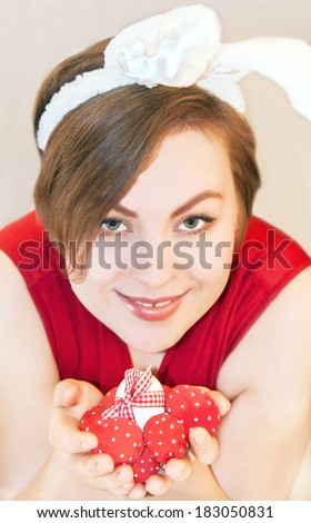 Portrait of a young woman wearing easter bunny ears. She is holding easter eggs. Indoor.