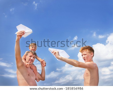 Happy caucasian sons and father with paper airplanes playing and smiling on sky background at the beach. Summer day. Outdoor. Copy space. Close up.