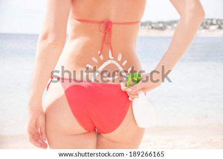 The sun drawing sunscreen (suntan lotion) on woman back. Caucasian girl in bikini is standing with plastic container on sunny beach. Close up, outdoor (Sharm El Sheikh, Egypt).