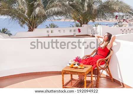 Caucasian resting woman is sitting and dreaming in a chair at the terrace with view on the sea. Relaxing beautiful young female model.  Image has copyspace for text. Outdoor (Sharm El Sheikh, Egypt).