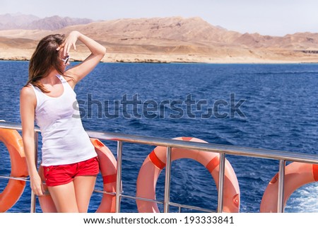 Attractive girl is relaxing on a yacht. Smiling happy female model in summer clothes is enjoying view  of ocean during travel holidays. Summer vacations concept. Copyspace (Sharm El Sheikh, Egypt).