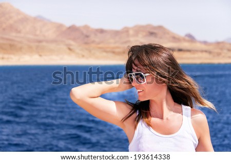Attractive girl is relaxing on a yacht. Happy female model in summer clothes is enjoying view of  ocean during travel holidays. Summer vacations concept. Copyspace (Sharm El Sheikh, Egypt).