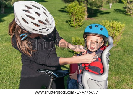Protection on the bicycle. Caucasian mother have biking helmet and putting biking helmet on outside to her son. The son is in the bicycle chair (seat) during bicycle ride. Travel concept.