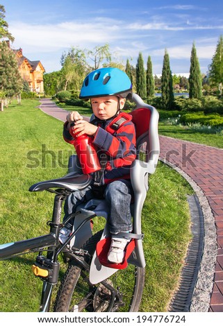 Protection on the bicycle. Baby boy is in the bicycle chair (seat) with a biking helmet on  head and bottle of water in hands during bicycle ride. Child has trip in the summer day. Travel concept.