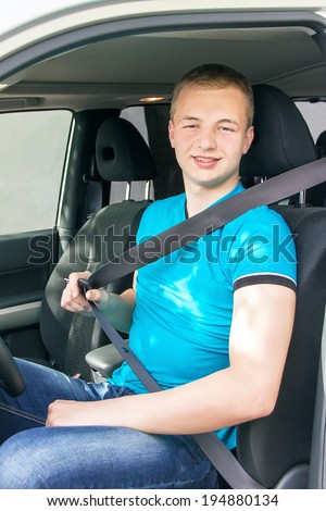 Car driver. Caucasian teen boy fastening seat belt in the car. Happy smiling young man behind the wheel. Vehicle and transportation concept. Close up, outdoor.