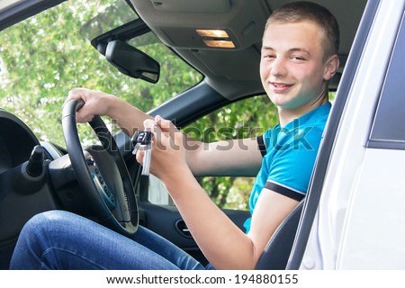 Car driver. Caucasian teen boy showing car key in the new car. Happy smiling young man behind the wheel. Travel and rental concept. Close up, outdoor.