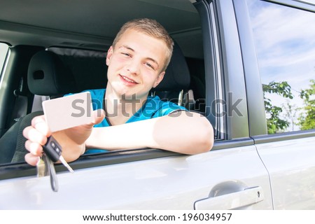 Car driver. Caucasian teen boy showing an empty white card for your message, new car key and car. Happy smiling young man behind the wheel. Travel and rental concept. Copy space, close up.