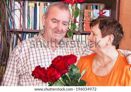 Mature couple. An upbeat joyful happy senior elderly couple in love with bouquet (bunch) of red roses at home. Greeting of birthday.