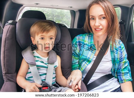Protection in the car. Caucasian cute son and mother are buckled with safety belt in a car.  Little boy is sitting in the car seat. Woman takes care about kid. Vehicle and transportation concept.