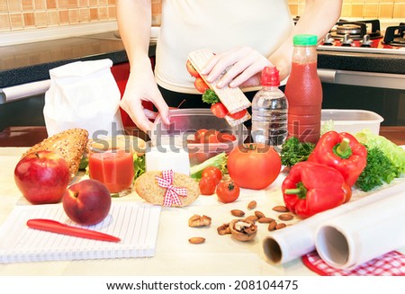 Hands of a woman is making school lunch box in the red color. It is more interesting for children. Caucasian female preparing food (fruits and vegetables) for healthy eating child (kid).