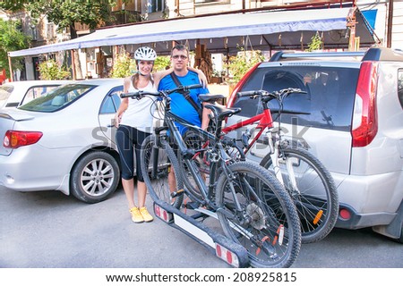 Smiling happy man and woman are standing near two bicycles mounted on trunk of car. Caucasian active tourists couple will ride bikes in the city. Travel (vacation) and adventure concept.