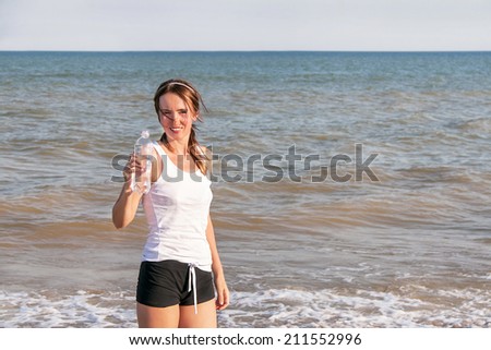 Active sport woman drinking water after exercising at the beach. Caucasian girl fitness model is at coast. Female athlete after work out in sunny light. Weight loss. Healthy lifestyle. Copy space.