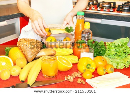 Hands of a woman is making school lunch box in the yellow  color. It is more interesting for children. Caucasian female preparing food (fruits and vegetables) for healthy eating child (kid).