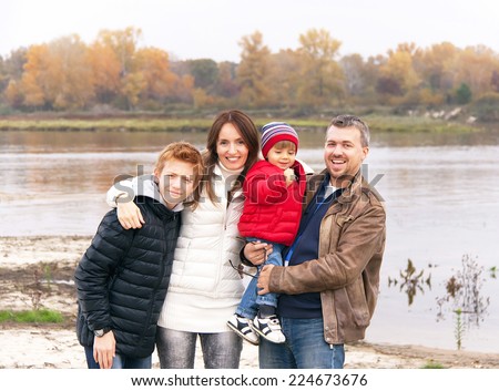 Family vacation. Caucasian happy family is standing and having fun by the river in the autumn day. Relaxing family on the autumnal beach - mother, father and two sons. Close up.