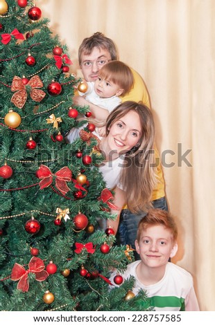 Portrait of happy smiling family by christmas tree. Caucasian family is standing and having fun. Relaxing, positivity family is in the room - mother, father and two sons. Close up. New year concept.