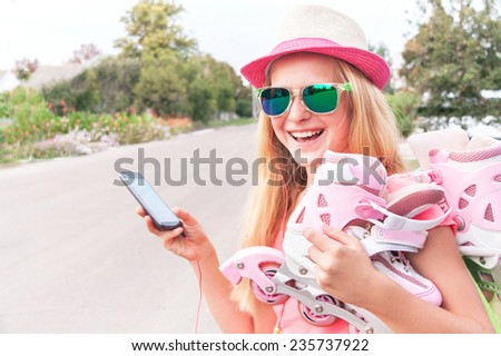 Teenager (girl) with roller skating shoes (inline skates) is using smart phone, listening music with headphone. Happy teen is wearing sunglasses and having fun. Concepts of technology, youth, sport.