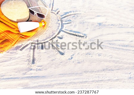 Sand texture (background) with hat, towel, sunscreen (suntan lotion, suncream), sunglasses on the a beach. The sun drawing in the sand. The empty pattern for message. Summer vacations. Copy space.