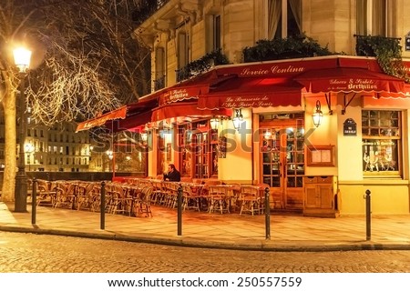 Paris, France - January 8, 2015. Traditional parisian cafe near famous Notre Dame de Paris in the evening. Wicker furniture is on the pavement. Travel (vacation),  cuisine concept. France.